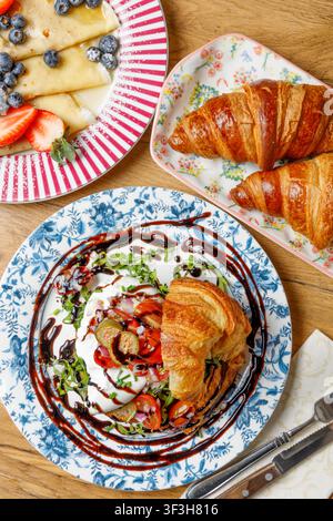 Prima piano di un croissant farcito con burrata mozzarella, pomodori e capperi, condito con salsa, su uno sfondo solido. Foto Stock
