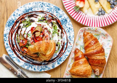 Prima piano di un croissant farcito con burrata mozzarella, pomodori e capperi, condito con salsa, su uno sfondo solido. Foto Stock