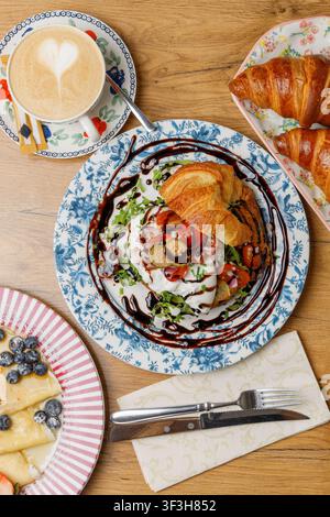 Prima piano di un croissant farcito con burrata mozzarella, pomodori e capperi, condito con salsa, su uno sfondo solido. Foto Stock