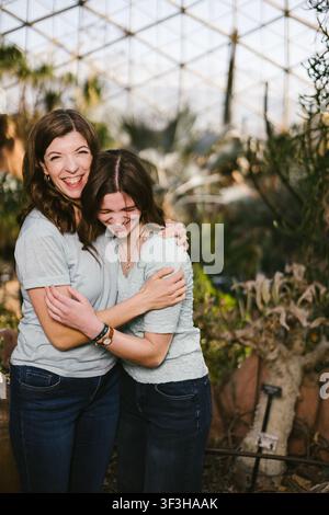 Madre e figlia che ridono e si abbracciano in una serra Foto Stock