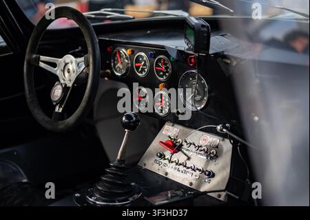 Vista dettagliata dell'interno di un'auto da corsa classica personalizzata con cruscotto dotato di strumenti analogici, pannello con interruttori a levetta e cambio manuale. Foto Stock