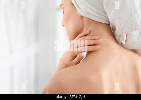 Giovane donna irriconoscibile avvolta in asciugamano idratando la sua pelle Foto Stock