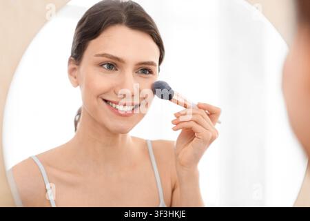 Closeup di attraente donna che applica arrossire sulla sua faccia Foto Stock