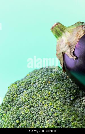 Una fotografia verticale in primo piano che mostra una foglia di broccolo fresca appoggiata contro una melanzana viola. L'immagine evidenzia la struttura complessa, simile a una foresta Foto Stock