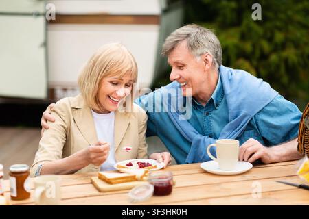Una coppia di anziani felice che ha toast con marmellata e caffè per la colazione al campeggio Foto Stock