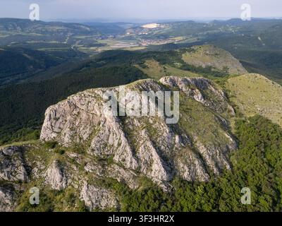 Ripresa aerea con drone ad angolo elevato della scogliera rocciosa Uch Kaya che si affaccia su valli verdi, foreste lussureggianti e paesaggi rurali in Bulgaria. Foto Stock