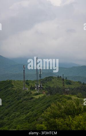 Diverse torri di telecomunicazione in piedi su colline verdi, collegano aree remote, contro un cielo nuvoloso, simboleggiando la comunicazione globale e la modernità Foto Stock