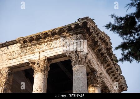 Pola, Croazia – 17 agosto 2025: Un primo piano ad angolazione bassa dell’antico tempio romano di Augusto a Pola, in Croazia. L’inquadratura mostra il dettaglio corinzio Foto Stock