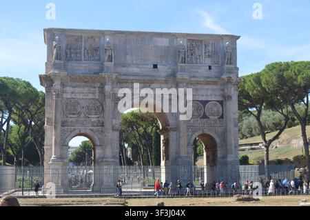 Una vista diurna soleggiata dell'iconico Arco di Costantino a Roma, con architettura romana antica, sculture e turisti che passano. Foto Stock
