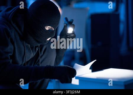 Ladro mascherato che tiene e legge documenti riservati Foto Stock