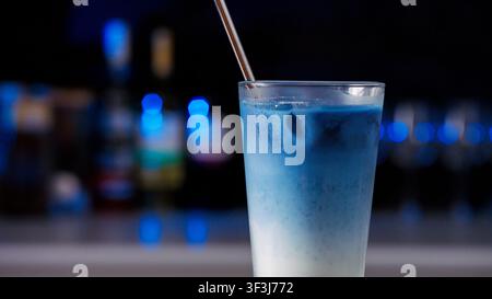 Bevanda blu raffreddata mescolata con latte servita in un bicchiere trasparente con cannuccia di metallo al bancone del bar di un nightclub Foto Stock
