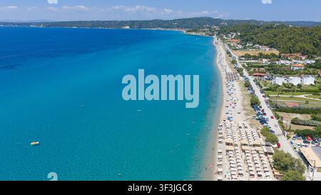 Spiaggia di Possidi, Grecia 11 luglio 2026. Prospettiva aerea di una lunga spiaggia sabbiosa fiancheggiata da ombrelloni accanto ad acque blu chiare e bagnanti sparsi. Foto Stock