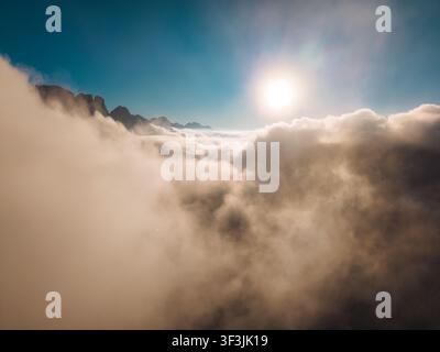 Sopra un mare di nuvole con l'alba che brilla su una cima montuosa frastagliata contro un cielo blu vivace Foto Stock