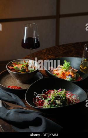 Fotografia professionale di alta qualità che mostra una tavola elegante da ristorante con tre piatti gourmet, microverdi e bicchieri di vino rosso e bianco Foto Stock