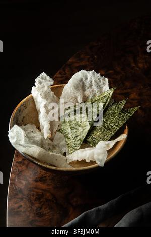 Foto professionale in primo piano di crostini di riso bianchi croccanti e fogli di alghe nori triangolari serviti in una ciotola di ceramica. Foto Stock