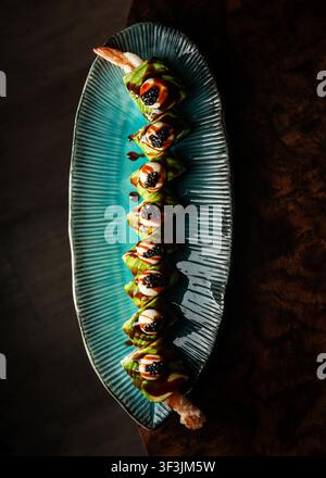 Fotografia professionale a vista dall'alto di rotoli di sushi drago gourmet guarniti con avocado e caviale su un piatto turchese. Foto Stock