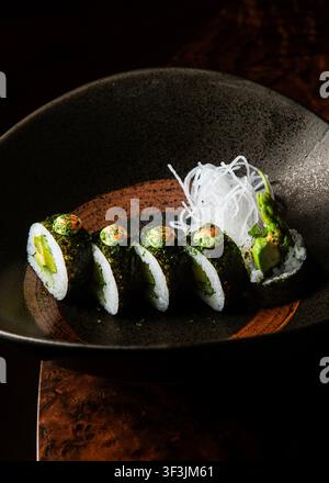 Vista laterale foto professionale di rotoli di sushi vegetali gourmet ripieni di asparagi e avocado, guarniti con salsa verde e ravanello daikon in Foto Stock