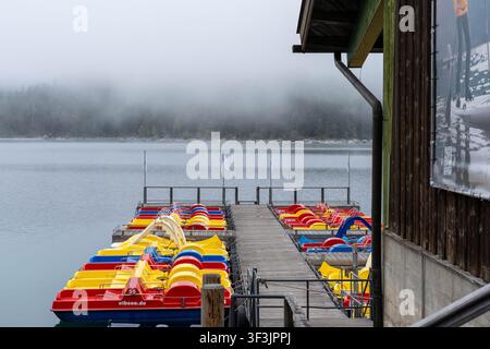 Garmisch-Partenkirchen Germania – 23 settembre 2025: Barche a remi ormeggiate sul lago Eibsee con la nebbia che avvolge la foresta vicina in Germania Foto Stock