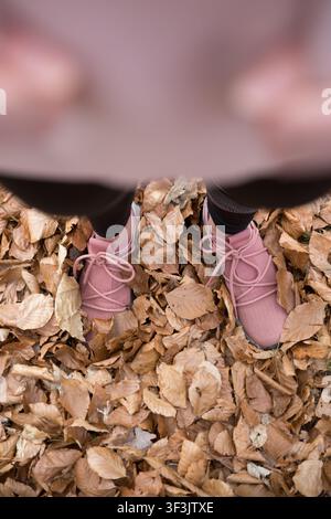 Un piano ad angolazione soggettiva (POV) dall'alto di una persona in piedi in un spesso tappeto di foglie secche cadute in autunno. Foto Stock