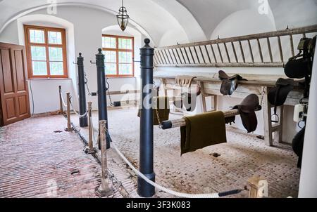 All'interno di una stalla storica conservata, che mostra selle vintage, coperte ed elementi architettonici rustici Foto Stock
