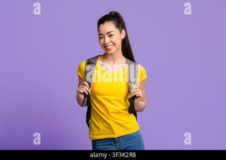 Giovane bella studentessa asiatica femminile con zaino in posa su viola Studio sfondo Foto Stock