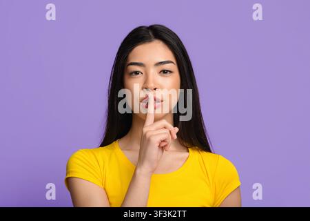 Shhh. Misteriosa giovane donna asiatica che mostra mantenere il segno del silenzio alla macchina fotografica Foto Stock