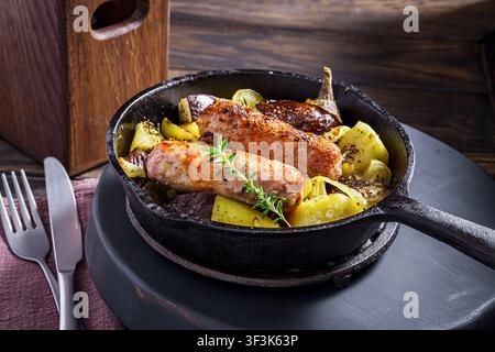 Salsicce di maiale con patate e melanzane vengono cotte in padella e servite con condimento. Foto Stock