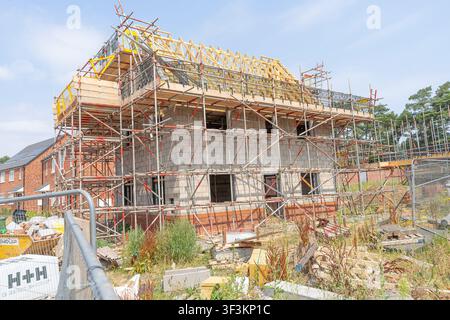Nuova casa in costruzione in un cantiere con una casa circondata da impalcature fino al colmo del tetto, detriti e bancali sparsi sotto l'edificio. Foto Stock