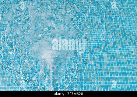 Prima vista di acqua blu chiara con bolle attive e increspature sul fondo della piscina piastrellato Foto Stock