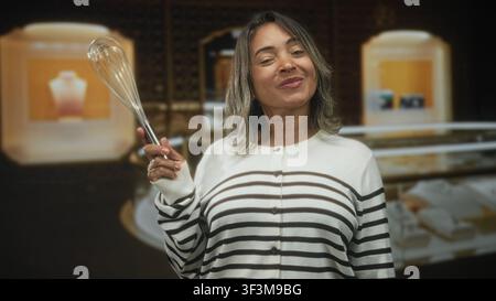 Donna ispanica tiene una frusta nella mano destra e sorride davanti alle vetrine di gioielli illuminate nello studio; gioia giocosa. Foto Stock