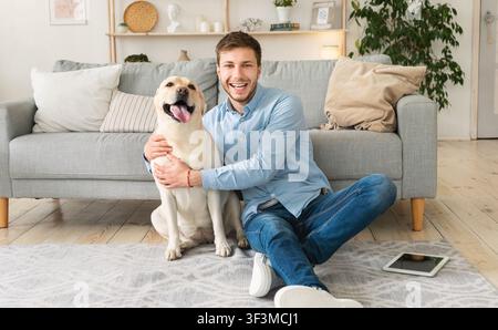 Giovane uomo felice con cane seduto sul pavimento Foto Stock