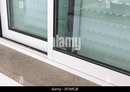 Vista ravvicinata di una finestra scorrevole incorniciata di bianco con vetri smerigliati e un davanzale in pietra strutturata Foto Stock