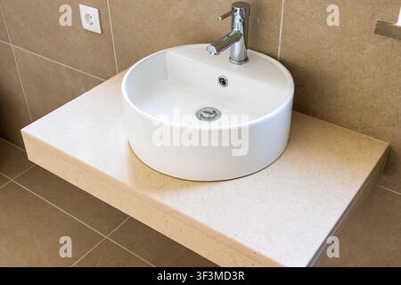Questa immagine mostra un lavandino rotondo ed elegante montato su un piano di lavoro minimalista, valorizzando l'estetica del bagno Foto Stock