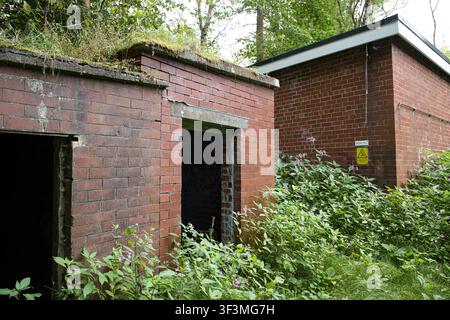 Edifici in mattoni rossi abbandonati e fatiscenti, ricoperti di vegetazione, strutture industriali, portali vuoti e cartello di avvertimento, Healey Dell, Rochdale, Regno Unito. Foto Stock