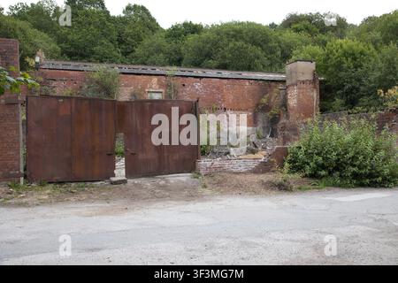 Edificio industriale in mattoni abbandonato e fatiscente a Healey Hall Mill a Rochdale, Regno Unito, con grandi porte doppie in metallo arrugginito. Foto Stock