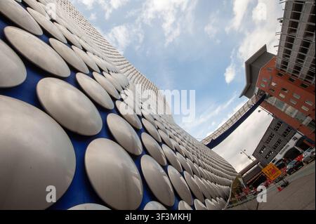 Vista ad angolo ampio, prospettiva bassa, che guarda lungo la facciata esterna a dischi argentati dell'edificio Selfridges verso Moor Street, Bullring, Birmingham, West Midlands, Inghilterra, fotografata il 6 maggio 2012. Progettata da Future Systems, l'iconica struttura di blobitecture domina a sinistra, con dischi in alluminio anodizzato su sfondo blu. Il ponte aereo superiore si collega con il parcheggio di Moor Street a destra, con traffico stradale e segnaletica sottostanti. Foto Stock