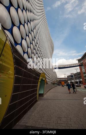 Vista verticale a livello stradale lungo il percorso pedonale lastricato accanto all'edificio Selfridges al Bullring, Birmingham, West Midlands, Inghilterra, scattata il 6 maggio 2012. Progettata da Future Systems, la struttura futuristica di blobitettura si erge con i suoi iconici dischi in alluminio anodizzato argentato, pannelli decorativi gialli curvi e ingressi stradali in vetro, che conducono verso il ponte sospeso e il parcheggio di Moor Street con pedoni che camminano davanti. Foto Stock