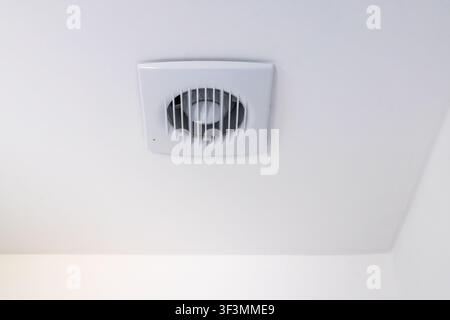 Una ventola di ventilazione bianca è montata a filo contro un soffitto bianco, fornendo circolazione d'aria in una stanza Foto Stock