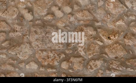 Una texture in primo piano di un muro di pietra medievale fatto di pietre rosse chiaro ruvide e arrotondate e di malta spessa. Foto Stock