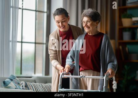 Momento caldo e gioioso tra una giovane donna premurosa e una signora anziana felice che usa un deambulatore in un soggiorno accogliente e illuminato dal sole. Questa immagine cattura magnificamente Foto Stock