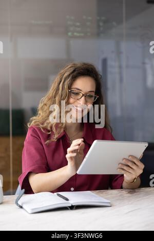 Donna d'affari sorridente che lavora su un tablet digitale in un ufficio aziendale Foto Stock