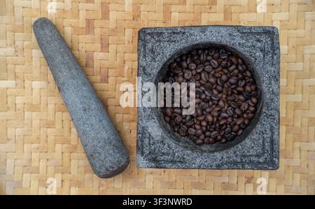 Grani di caffè tostati in mortaio di pietra con pestello su stuoia di bambù Foto Stock