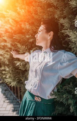 Donna tramonto siepe giovane donna in camicetta bianca appoggiata contro lussureggianti cespugli del giardino durante la luce dell'ora dorata Foto Stock
