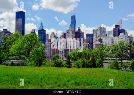 New York City, USA – 1 giugno 2026: Architettura di New York e vista sullo skyline dei grattacieli monumentali dal prato verde di Roosevelt Island. Foto Stock
