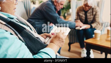 Mani, anziana e lettura a casa con cruciverba, ricerca di parole e quiz per la salute. Persona anziana, scrittura e libro a casa con giochi di sudoku Foto Stock