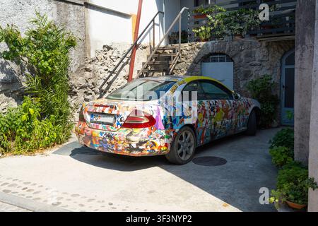 Podgorica, Montenegro. 20 luglio 2026. Un’auto è coperta da una pellicola adesiva colorata e intricata con numerosi personaggi dei cartoni animati. Il veicolo è parcheggiato Foto Stock