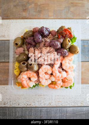 Insalata di frutti di mare mediterranea fresca con gamberetti cotti, tonno in scatola, olive nere di Kalamata e verdi, pasta ed erbe in un contenitore di plastica trasparente da asporto Foto Stock