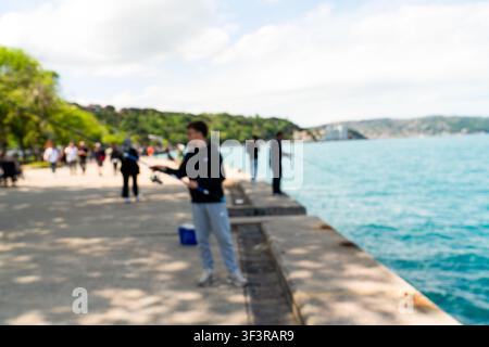 Vista sfocata di persone che pescano e passeggiano lungo la promenade del Bosforo a Istanbul in una giornata soleggiata Foto Stock