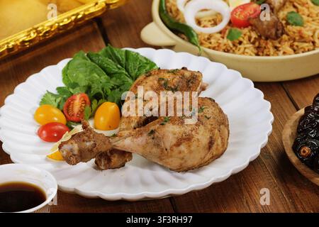 Pollo grigliato tradizionale mediorientale Dajaj Mashwi servito con insalata fresca, pomodorini e riso speziato su tavolo di legno. Foto Stock