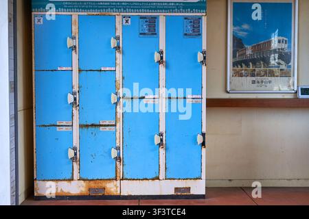 Una fila logorata di nove armadietti blu a gettone disposti in una griglia tre per tre, che mostrano ruggine e età significative, situata in una Foto Stock